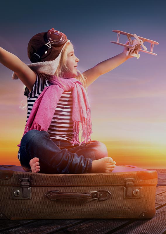 A kid sits on a suitcase playing with a toy plane