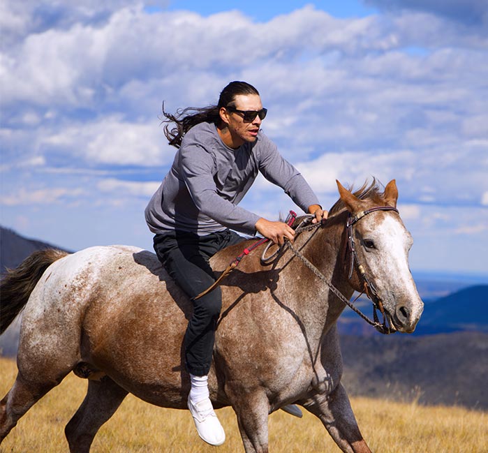 A man on horseback rides through yellow grass.